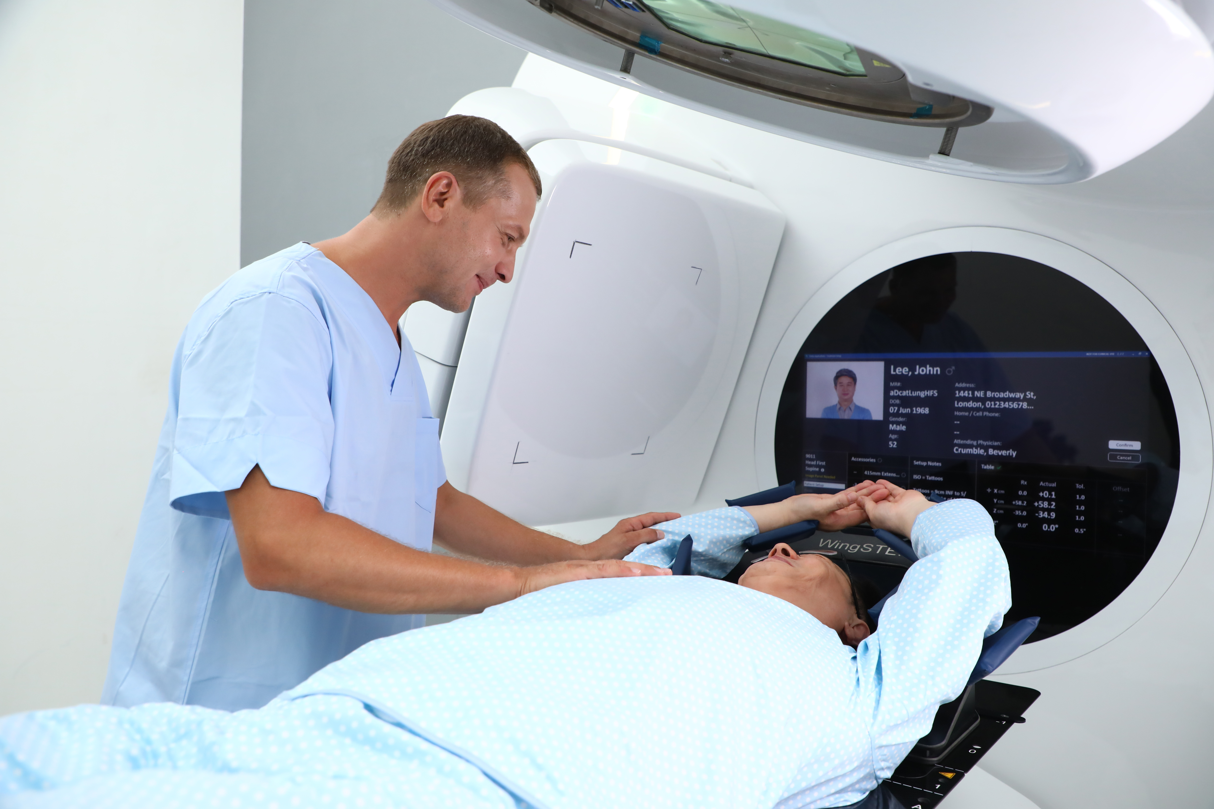Therapist tending to a patient on an Elekta Harmony Linac with the Treatment Setup workspace displayed on the machine's central screen.
